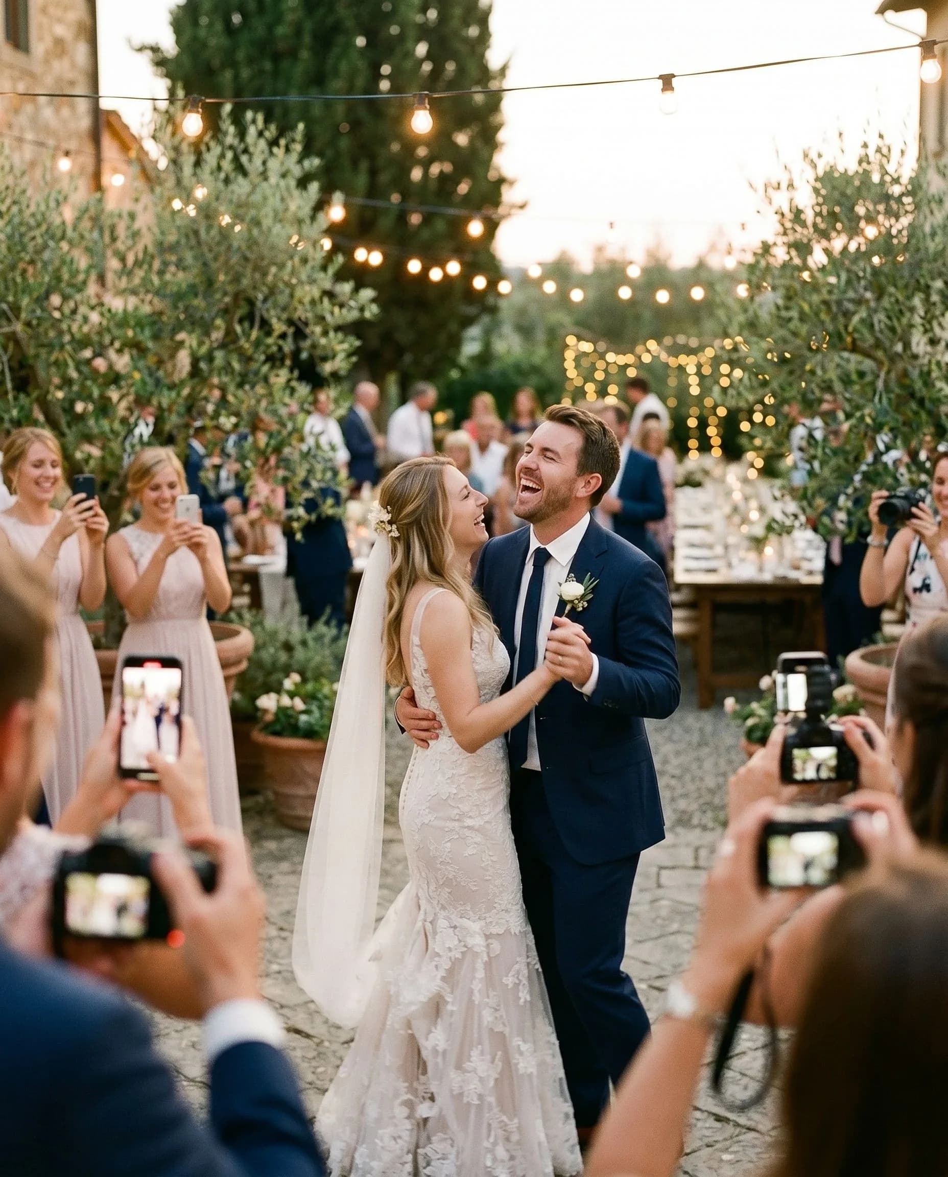 Recém-casados rindo no meio da dança enquanto os convidados os fotografam com seus celulares